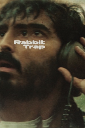 A man with a beard and intense expression listens with headphones. The words “Rabbit Trap” are overlaid. The mood is focused and mysterious.